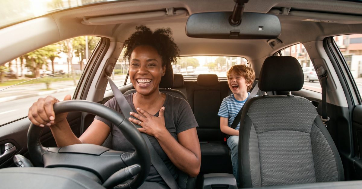 A mother laughing while driving, with her son laughing in the back seat